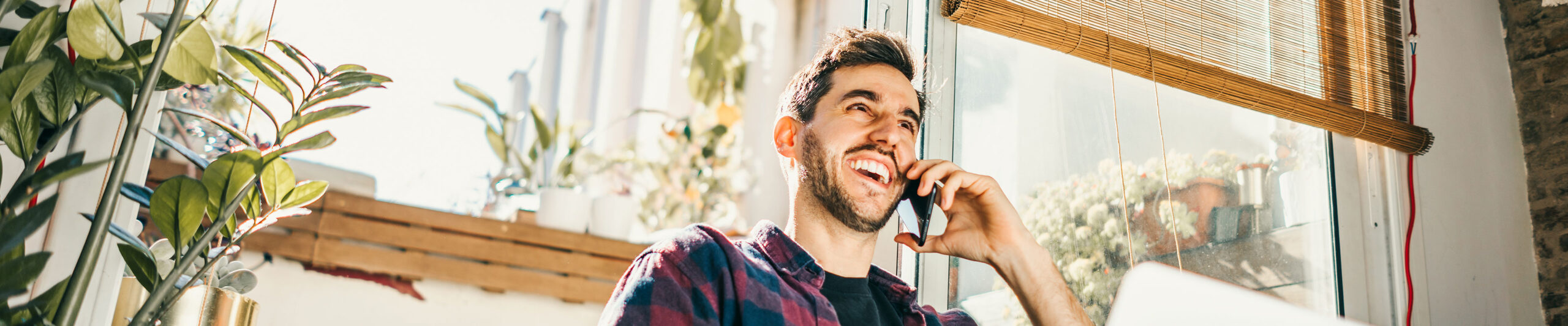 A man smiles and laughs while talking on the phone while sitting in his living room.