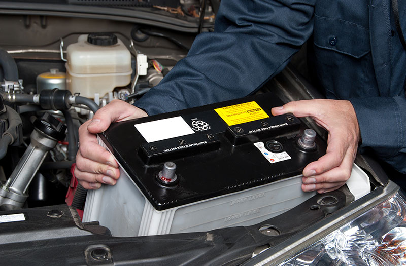 an image showing a car technician inserting a battery into a car