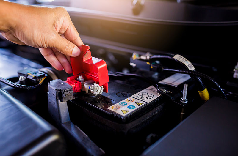an image of a person lifting up the red terminal cover on a battery