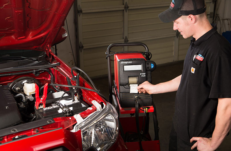 an image of a United Battery employee standing next to a red car, and using a device to test the battery