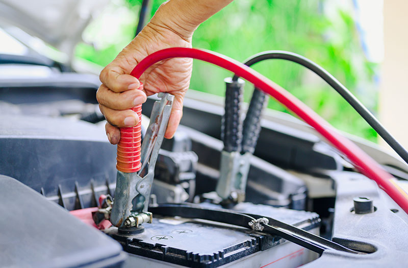 Someone connecting terminals on a car battery to charge it.