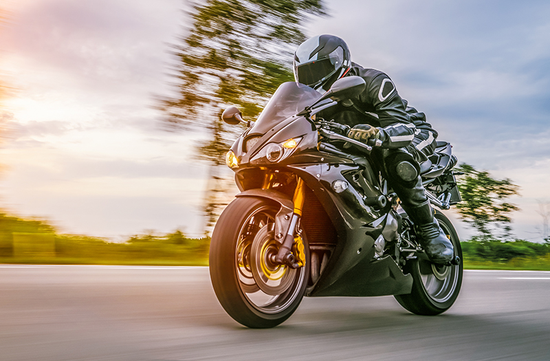 A person rides a sport motorcycle while wearing a full leather racing suit.